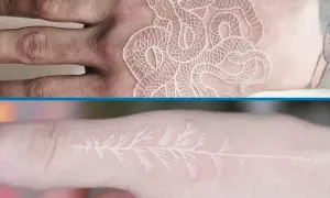Un delicado tatuaje blanco de serpiente enredada en una mano y una rama de árbol en un dedo.