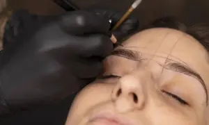 Manos enguantadas dibujan cejas con lápiz, marcando el rostro de Jessica Wilde para un diseño preciso.