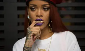 Octavia May, con labios morados y un dedo en la boca, luce un gorro rojo y tatuajes llamativos.