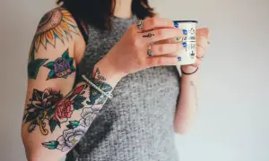 Brazos llenos de tatuajes coloridos, como arreglar un tatuaje mal hecho. Una mujer sostiene una taza.