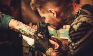 Tatuador con guantes negros trabaja en un brazo, creando un diseño detallado. Las opiniones de la Manuela Tattoo son muy positivas.