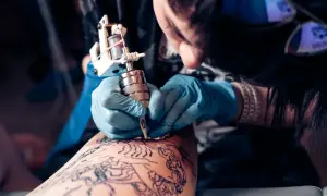 Artista tatuando en la convención de tatuajes Valencia. Manos enguantadas trabajan con precisión sobre un diseño en la piel.