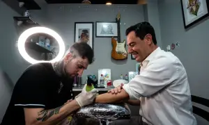 Un hombre sonriente recibe un tatuaje de un artista con estilo, considerado el mejor tatuador del mundo.