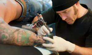 Artista tatuador concentrado, usando la mejor tinta para tatuajes en un brazo con diseños coloridos.