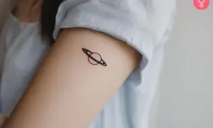 Tatuaje minimalista de Saturno en el brazo. Tatuarse Saturno puede simbolizar madurez, responsabilidad y el paso del tiempo.