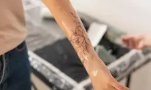 Brazo con un diseño de flores en proceso de tatuaje. El artista aplica una loción, similar a los cuidados post-tatuajes médicos, para hidratar la piel.