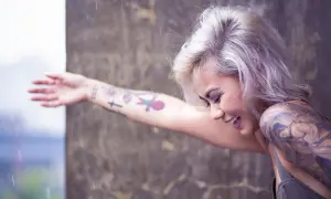 Mujer sonríe bajo la lluvia, con su brazo lleno de tatuajes, recordando el día que decidió hacerse un tatuaje.