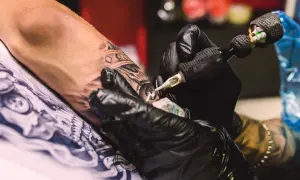 Manos enguantadas crean arte en la piel, un detalle de la **convención tatuajes**.