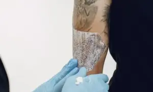 Manos enguantadas aplican Bepanthol sobre un tatuaje para ayudar a su curación.