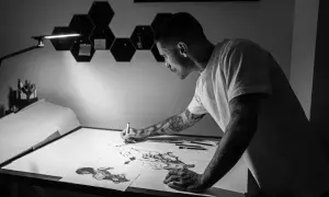 Víctor del Fueyo, artista con tatuajes, dibuja con concentración bajo una lámpara.