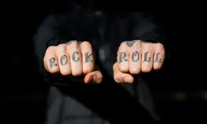 Manos con tatuajes en los nudillos que dicen "ROCK ROLL". A pesar de la pena y el pánico, el rock and roll vive.
