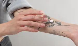 Mano aplicando crema sobre un tatuaje de flores en el antebrazo.