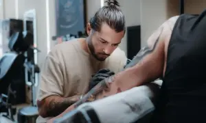 Toni Nova, un artista del tatuaje, trabaja con concentración en el brazo de un cliente.