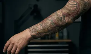 Brazo con tatuajes de dragones, simbolizando fuerza y sabiduría. El diseño detallado muestra escamas doradas y rojas, garras afiladas y nubes estilizadas, reflejando el profundo significado de los tatuajes de dragones.