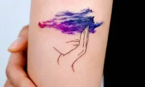 Tatuaje de una mano sosteniendo una nube morada y azul, simbolizando la superación de la ansiedad.