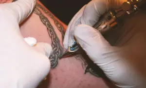 Manos enguantadas tatuando una cadena rota en la piel.