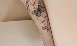 Un delicado tatuaje de mariposa y flores silvestres en un brazo, simbolizando la libertad y la belleza efímera.