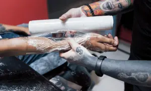 Man wrapping a fresh tattoo with plastic wrap. La curación es clave, y te preguntarás cuántos días hay que ponerse crema en un tatuaje para que quede perfecto.