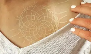 Un delicado tatuaje white out con diseño de atrapasueños en la clavícula.