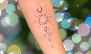 Brazo con tatuaje de sol, luna y símbolo unamalo, representando protección y tatuajes espirituales.
