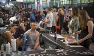 En la convencion tattoo barcelona, un artista tatúa un brazo mientras otros observan diseños.