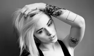 Alysha Nett, con su cabello rubio y tatuajes llamativos, posa con una mano en su cabeza.