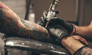 Primer plano de un brazo con tatuajes coloridos siendo tatuado por una máquina.