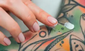 Dedos aplicando crema sobre un tatuaje colorido, parte de un proceso de cuidado y tatuaje terapéutico.
