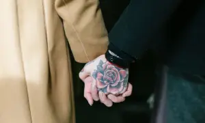 Manos entrelazadas, una con un tatuaje de rosa roja, mostrando el arte de los tatouages homme.