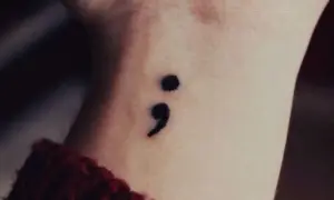 Un delicado tatuaje de punto y coma en la muñeca, símbolo de esperanza y resiliencia.