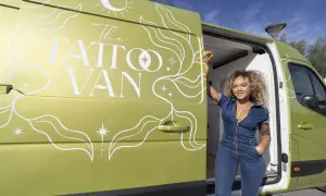 Una mujer sonriente posa junto a una furgoneta verde decorada con "The Tattoo Van". ¡Un estudio de tatuajes camper listo para viajar!