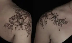 Delicados blackwork tattoos de flores y hojas adornan los hombros, creando un diseño botánico elegante y atemporal.