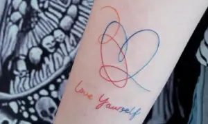 Tatuajes de corazón y "Love Yourself" en el brazo, un símbolo de fortaleza y amor propio.
