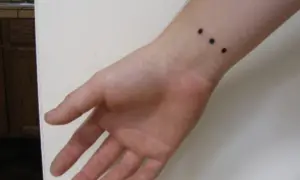 Muñeca con un discreto tatuaje de tres puntos negros alineados.