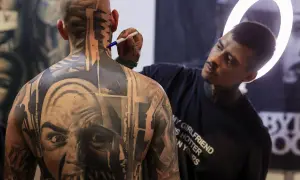 Artista de **val tattoo** retocando un intrincado diseño en la nuca de un hombre.