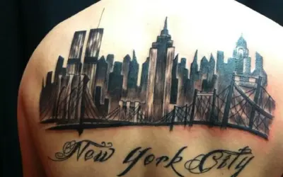 Tatuaje de un horizonte de Nueva York con puentes y el texto "New York City" en caligrafía.
