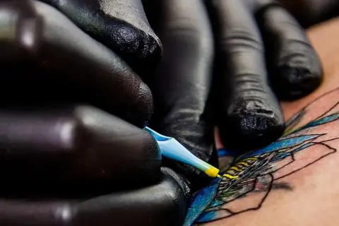 Manos enguantadas crean arte en piel, un detalle de los mejores tatuadores de España.