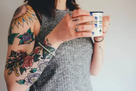 Brazos llenos de tatuajes coloridos, como arreglar un tatuaje mal hecho. Una mujer sostiene una taza.