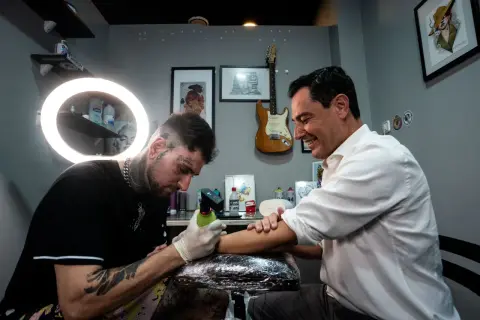 Un hombre sonriente recibe un tatuaje de un artista con estilo, considerado el mejor tatuador del mundo.