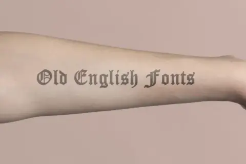 Brazo con tatuajes de letras góticas, "Old English Fonts", que parecen obras de arte permanentes.