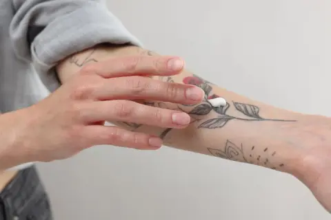 Mano aplicando crema sobre un tatuaje de flores en el antebrazo.