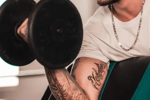 Hombre con tatuaje levanta pesa, mostrando su dedicación al deporte y su arte corporal.