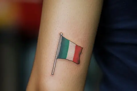 Un tatuaje de la bandera de Italia ondea en un brazo, un recordatorio permanente de la belleza y la cultura de ese país.