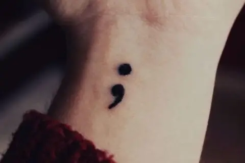 Un delicado tatuaje de punto y coma en la muñeca, símbolo de esperanza y resiliencia.