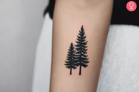Tatuaje de dos pinos negros en un brazo, simbolizando la fuerza y el crecimiento del bosque.