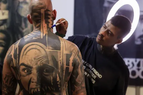 Artista de **val tattoo** retocando un intrincado diseño en la nuca de un hombre.