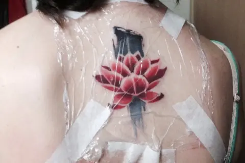 Flor de loto roja y azul recién tatuada en la espalda, cubierta con plástico y cinta. ¿Cuánto se tarda en hacer un tatuaje?