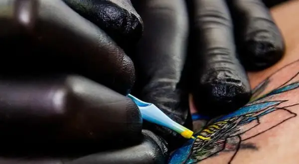 Manos enguantadas crean arte en piel, un detalle de los mejores tatuadores de España.