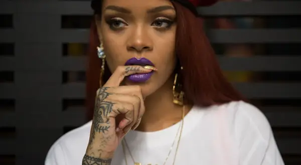 Octavia May, con labios morados y un dedo en la boca, luce un gorro rojo y tatuajes llamativos.