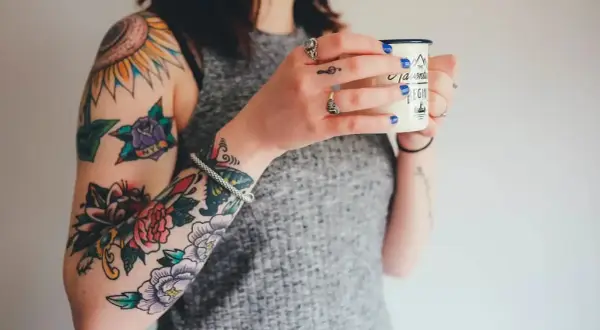 Brazos llenos de tatuajes coloridos, como arreglar un tatuaje mal hecho. Una mujer sostiene una taza.